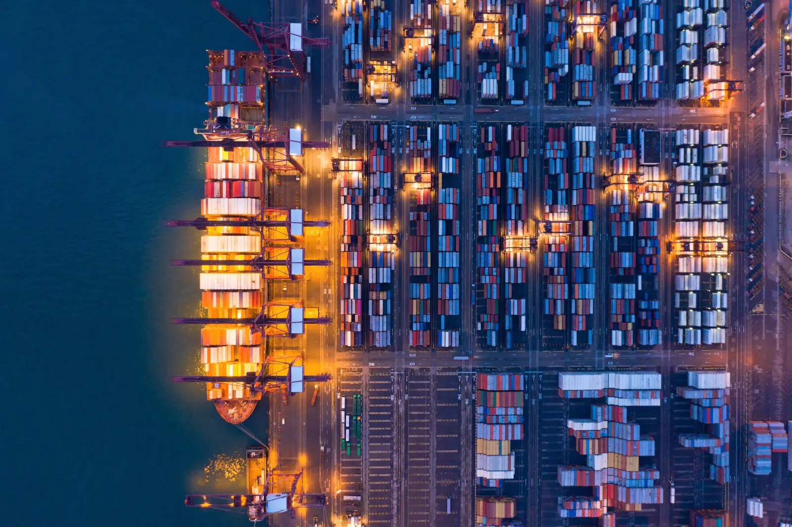 Luftaufnahme eines Containerschiffs und eines Containerterminals bei Nacht